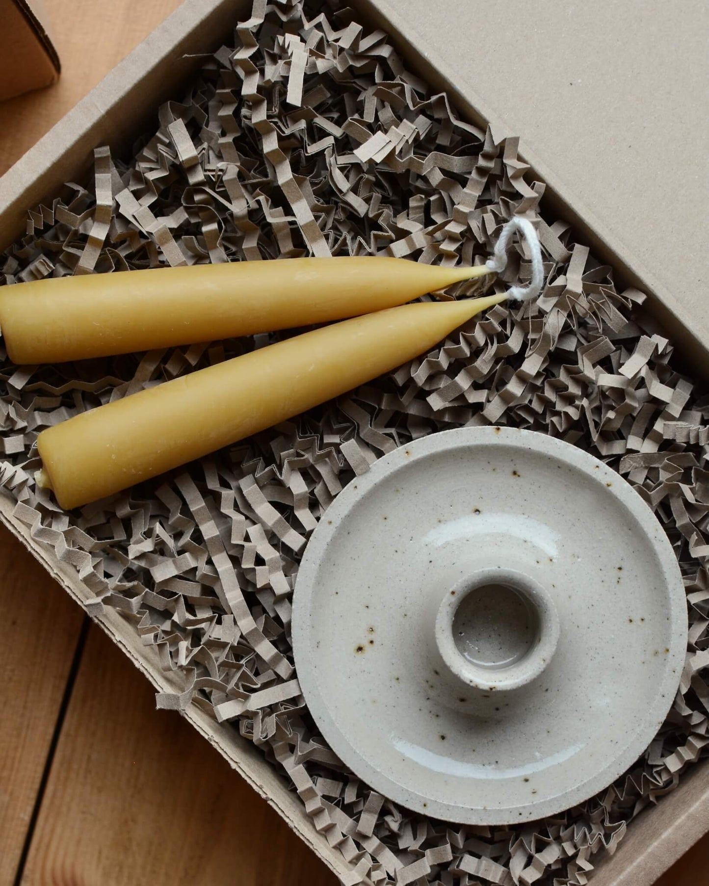 A gift box, containing a pair of taper beeswax candles and a ceramic candle holder.