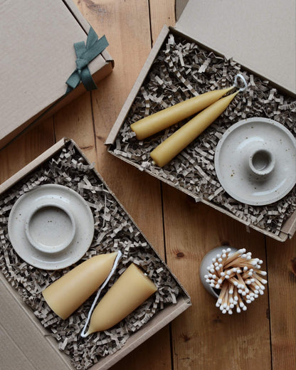 A pair of gift boxes, containing beeswax candles and ceramic candle holders.