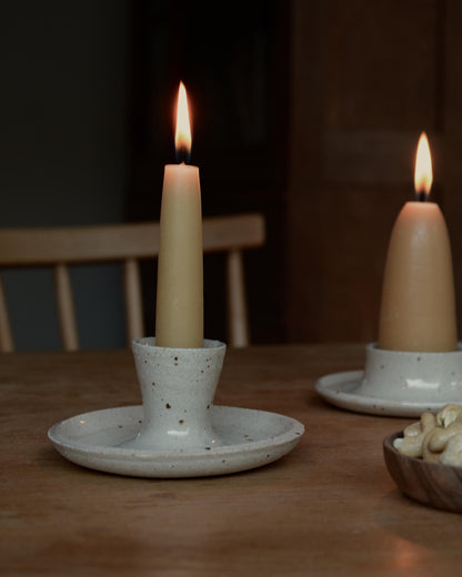 A lit beeswax candle, in a ceramic candle holder.