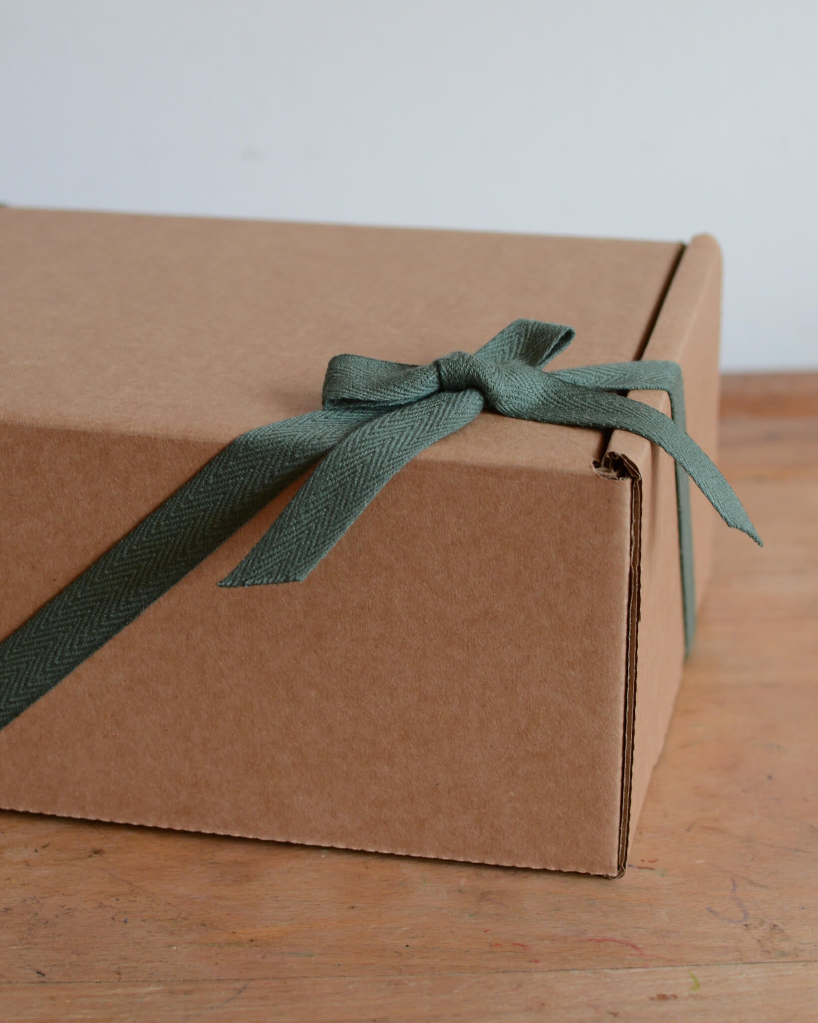 A kraft gift box with a green ribbon, tied into a bow.