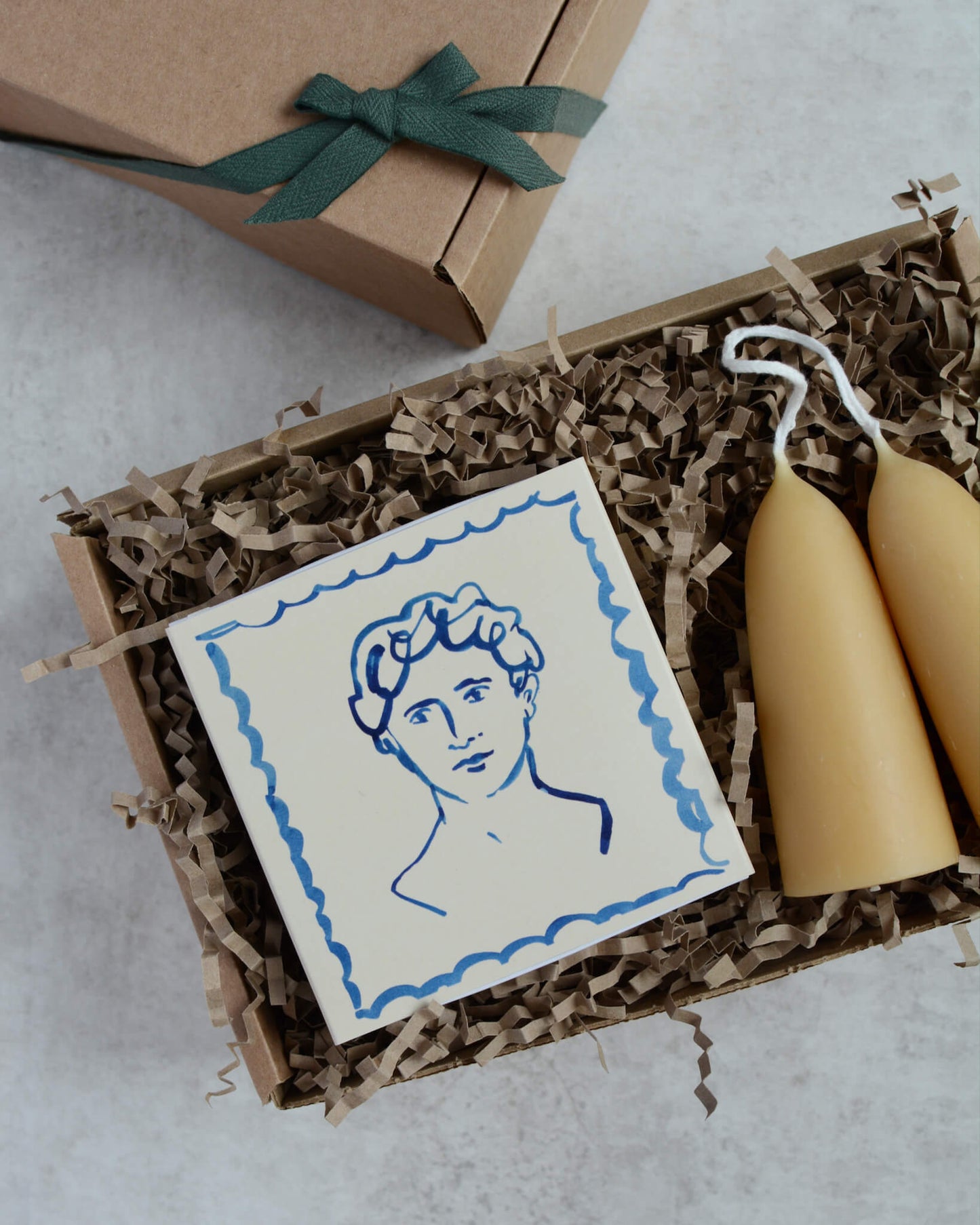 A gift box containing a pair of stubby beeswax candles and a matchbox with the illustration of a man.