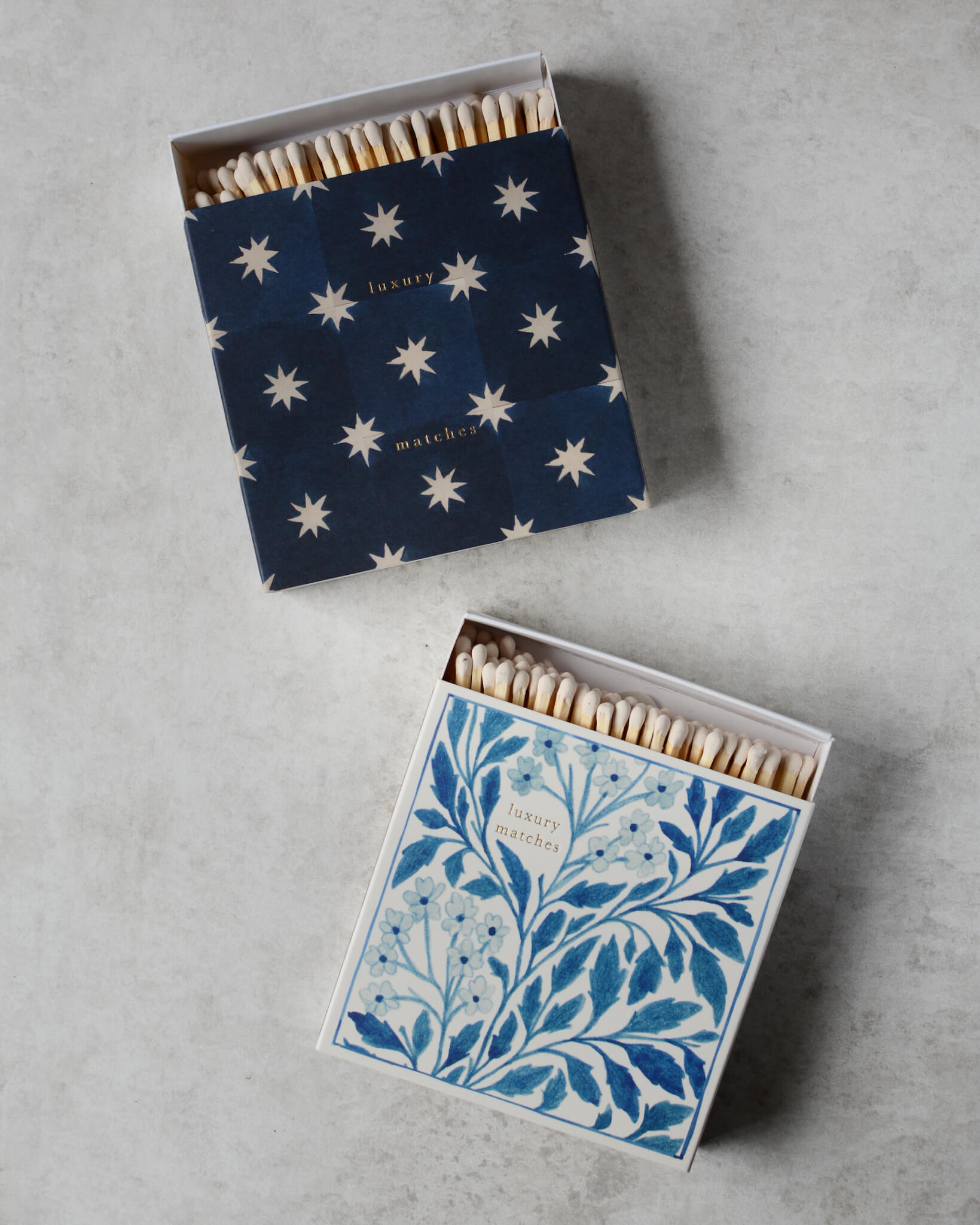 A pair of blue and white match boxes, with a star tile print on one and a floral illustration on the other.