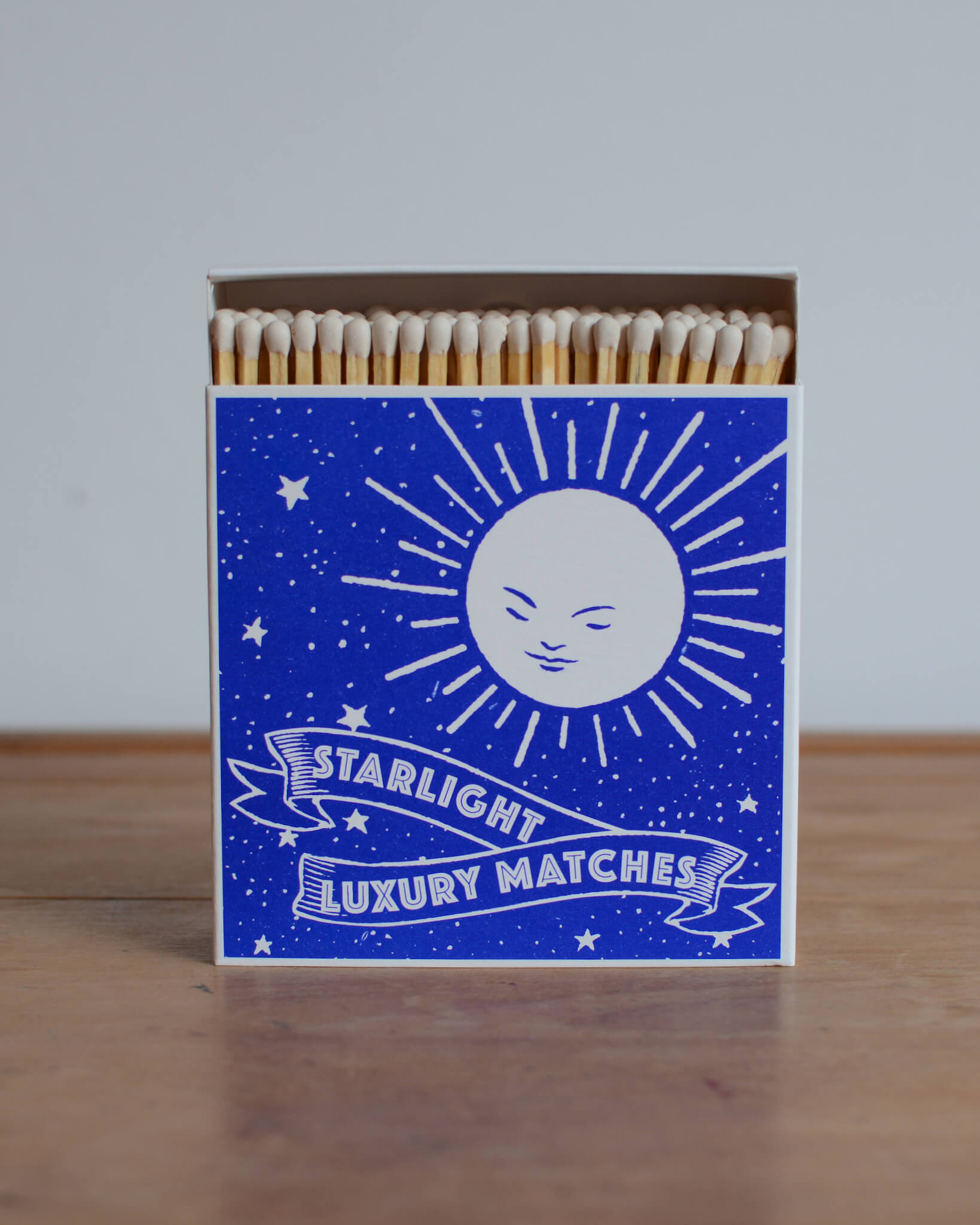 A blue matchbox with a white illustration of the moon and white lettering.