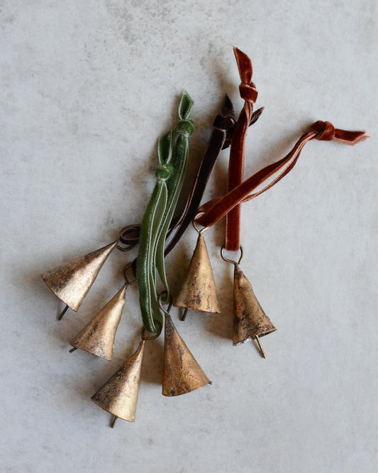 Brass bell Christmas ornaments, strung with velvet ribbon in rich tones.