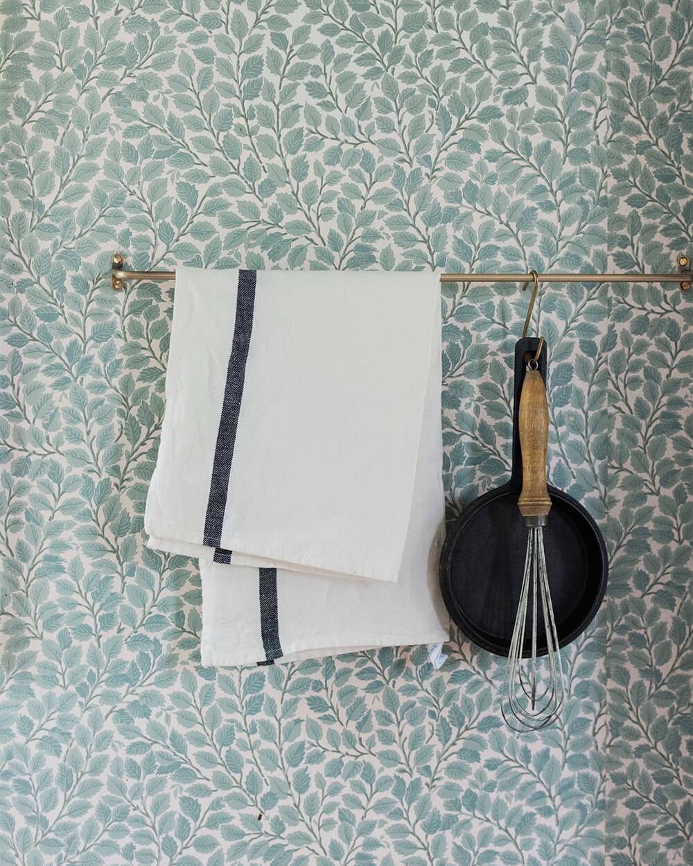 A solid brass hanging rail, holding kitchen utensils and tea towel.