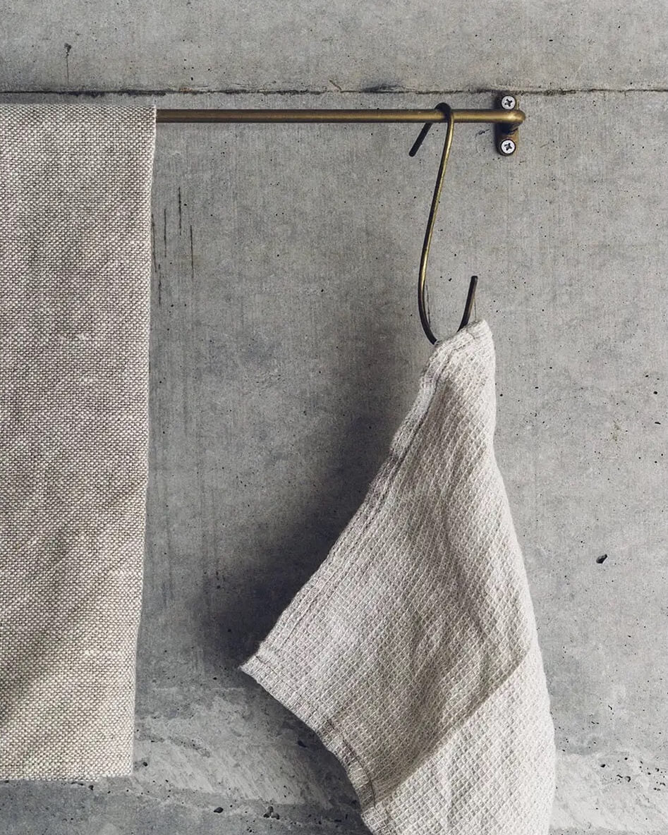 A brass hanging rail and 'S' shape hook, holding a tea towel.