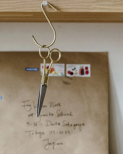 A pair of brass scissors hanging from a brass 'S' shaped metal hook.