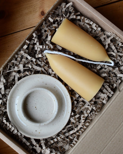 A pair of a stubby beeswax candles, in a gift box with a ceramic candle holder.