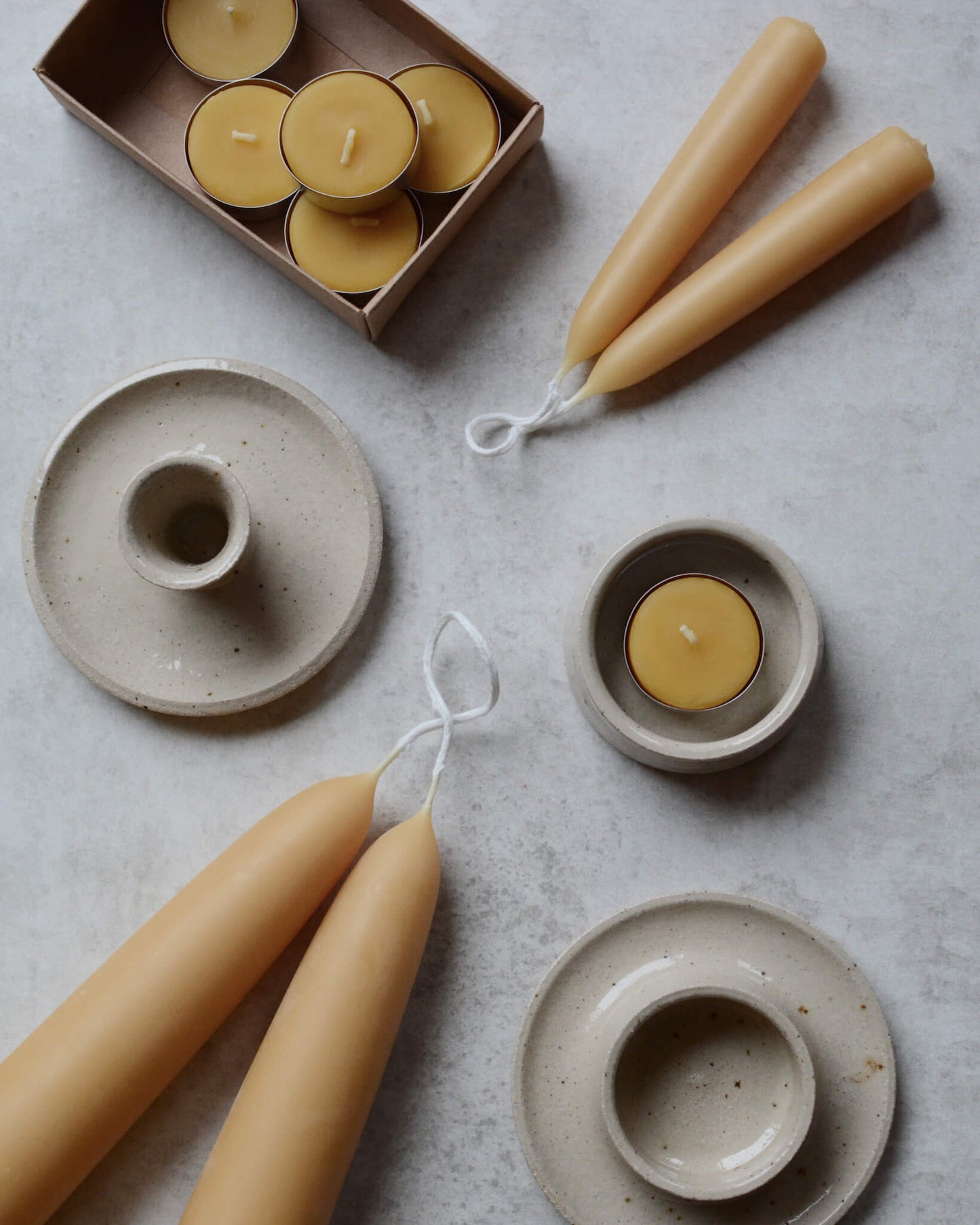 A collection of beeswax candles and tea lights, with ceramic candle holders.