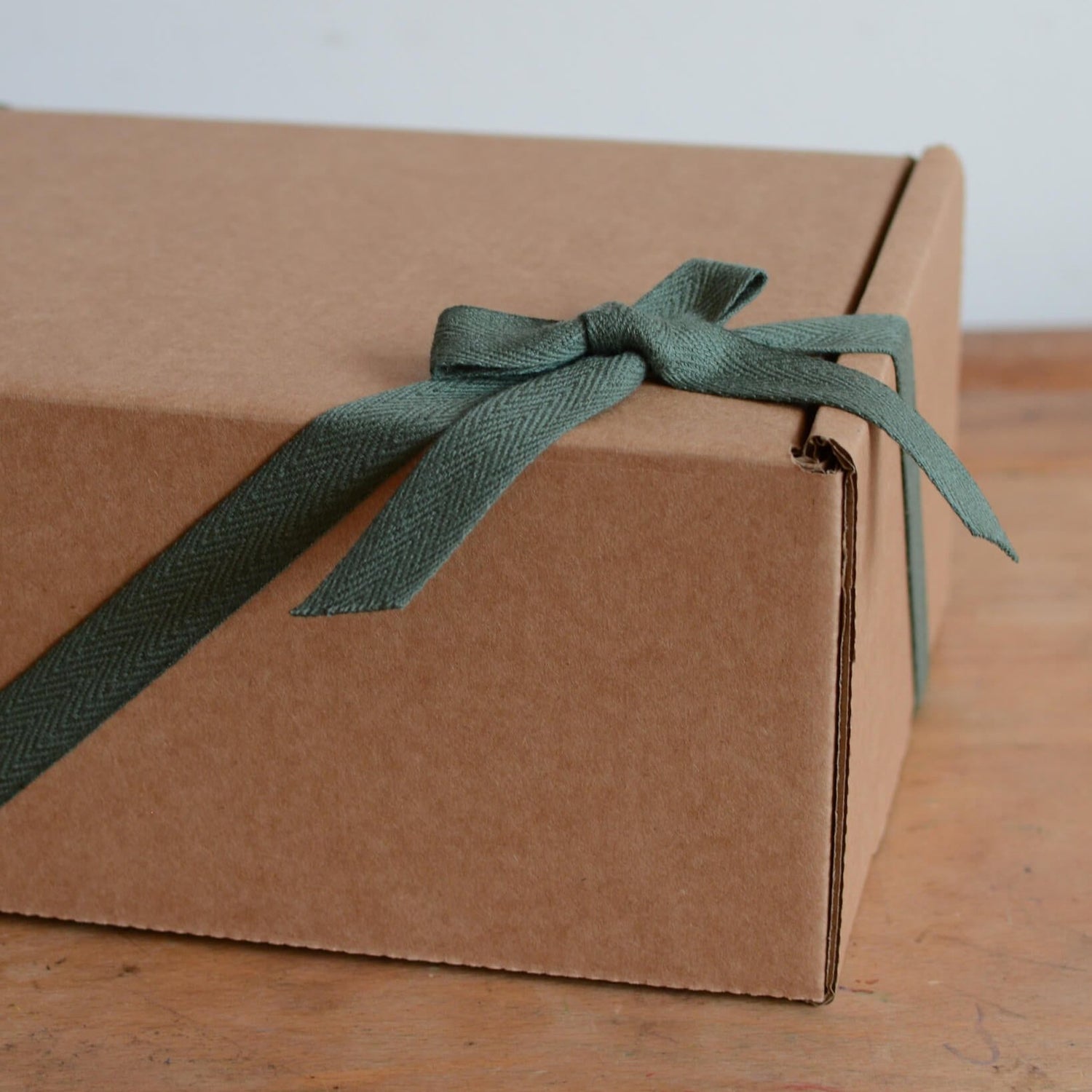 A kraft gift box, tied with a green cotton bow.