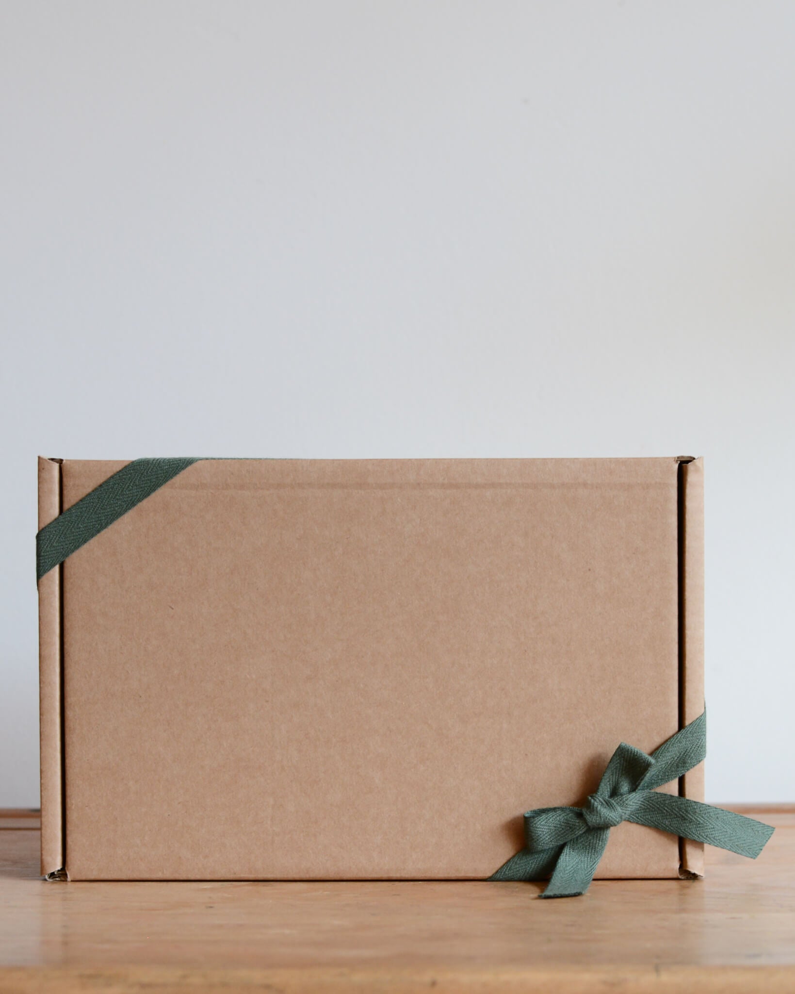 A kraft gift box, tied with a green cotton bow.