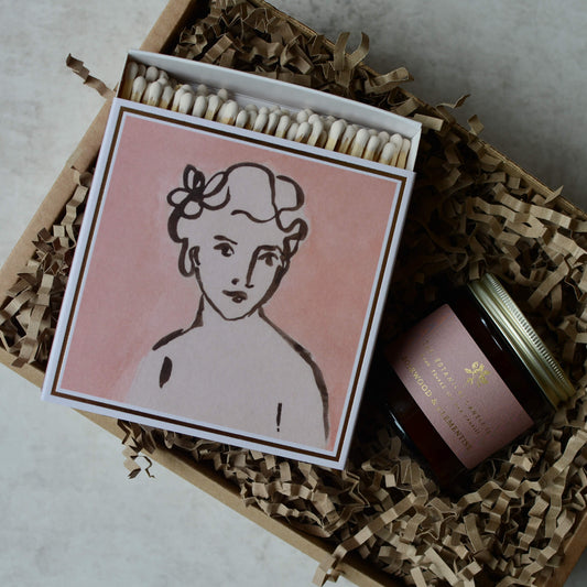 A pink gift box, containing a rosewood & clementine candle and a box of letterpress matches.