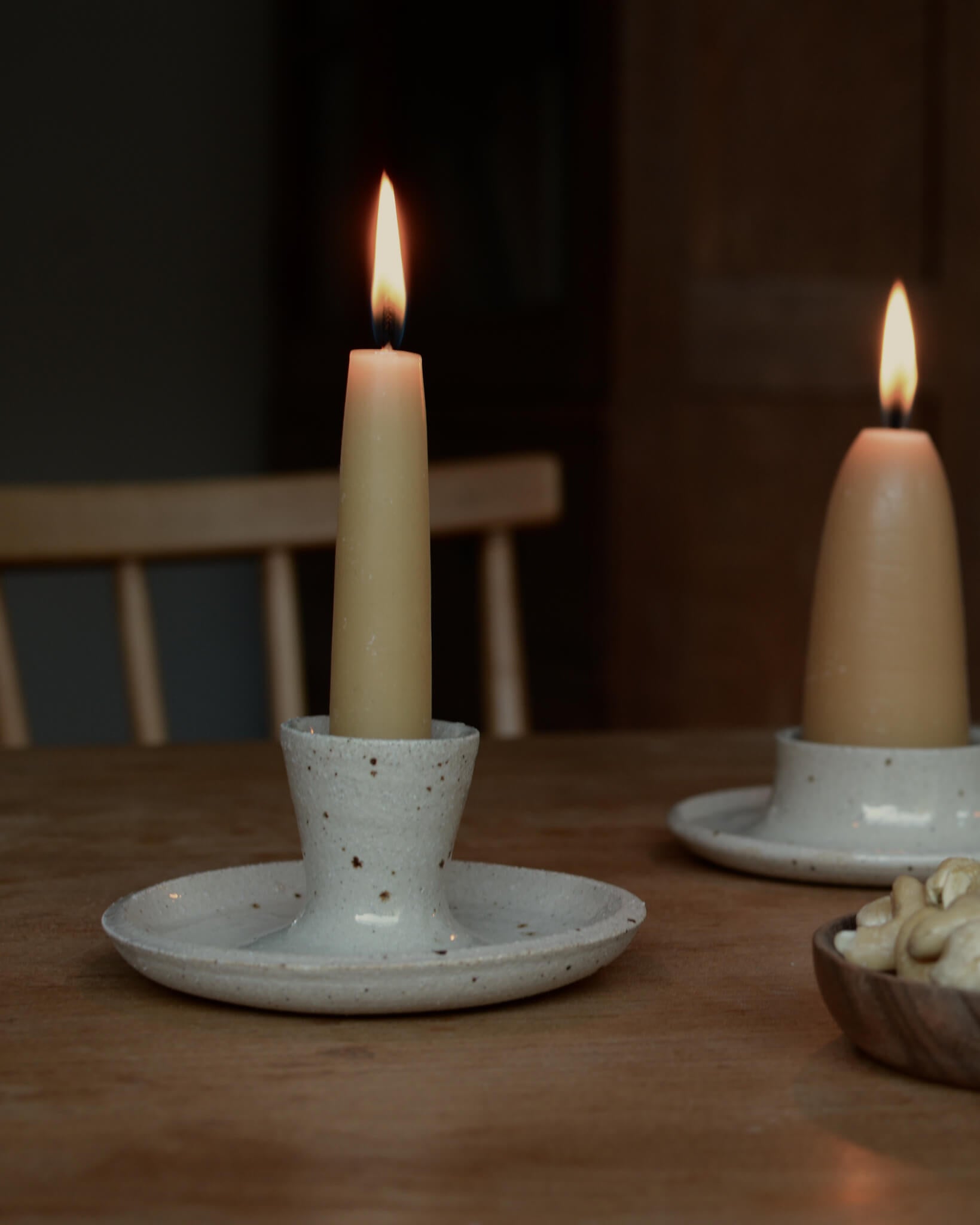 Oatmeal coloured ceramic candle holders and beeswax candles, on a table top.