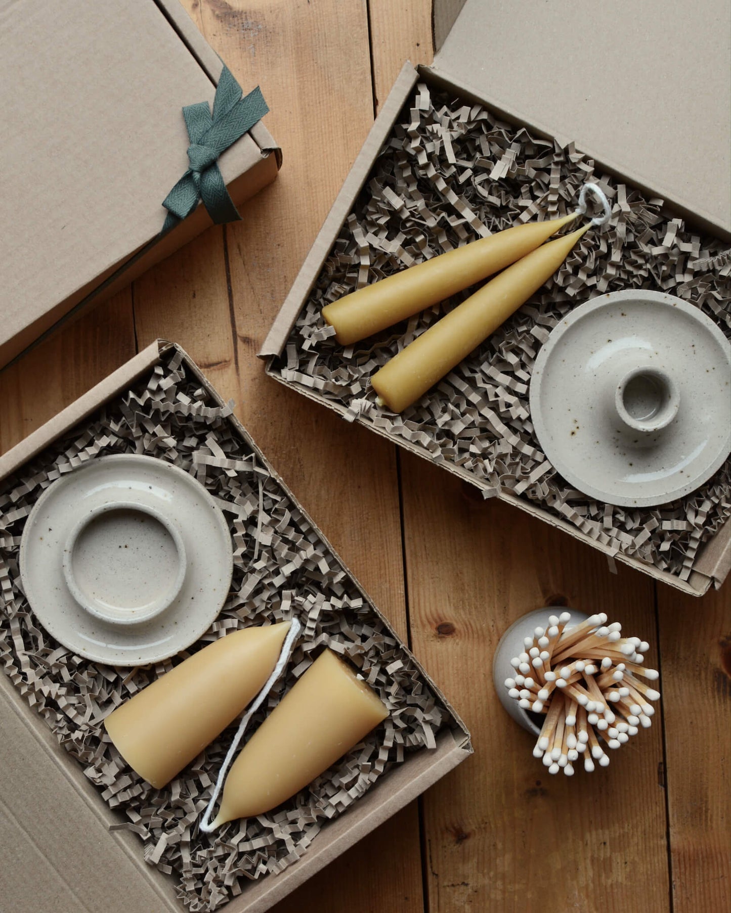 A pair of gift boxes, containing ceramic candle holders and beeswax candles.