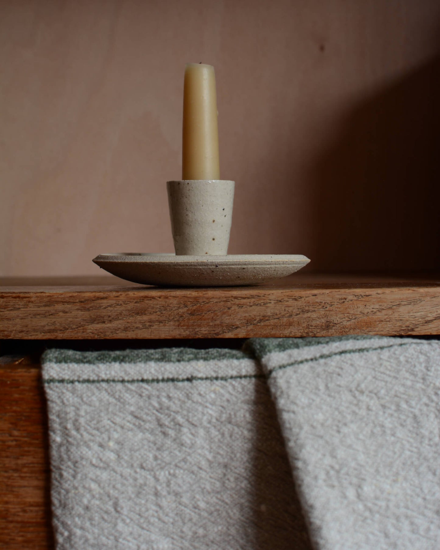 An oatmeal coloured ceramic dinner candle holder and a beeswax candle.