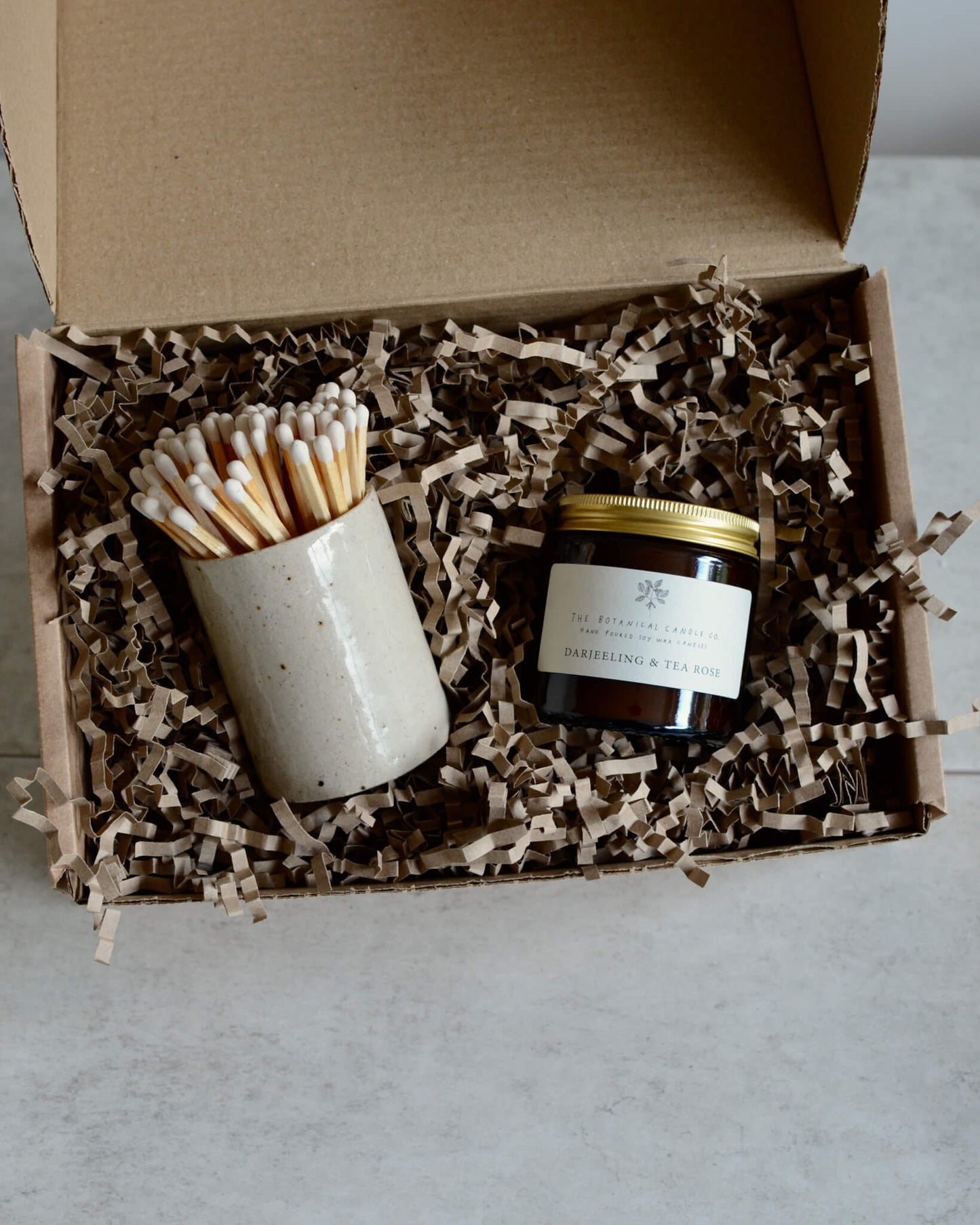 An oatmeal ceramic match pot with matches and a glass jar candle, in a gift box.