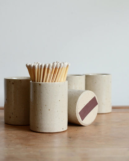 A collection of oatmeal ceramic match pot with matches.