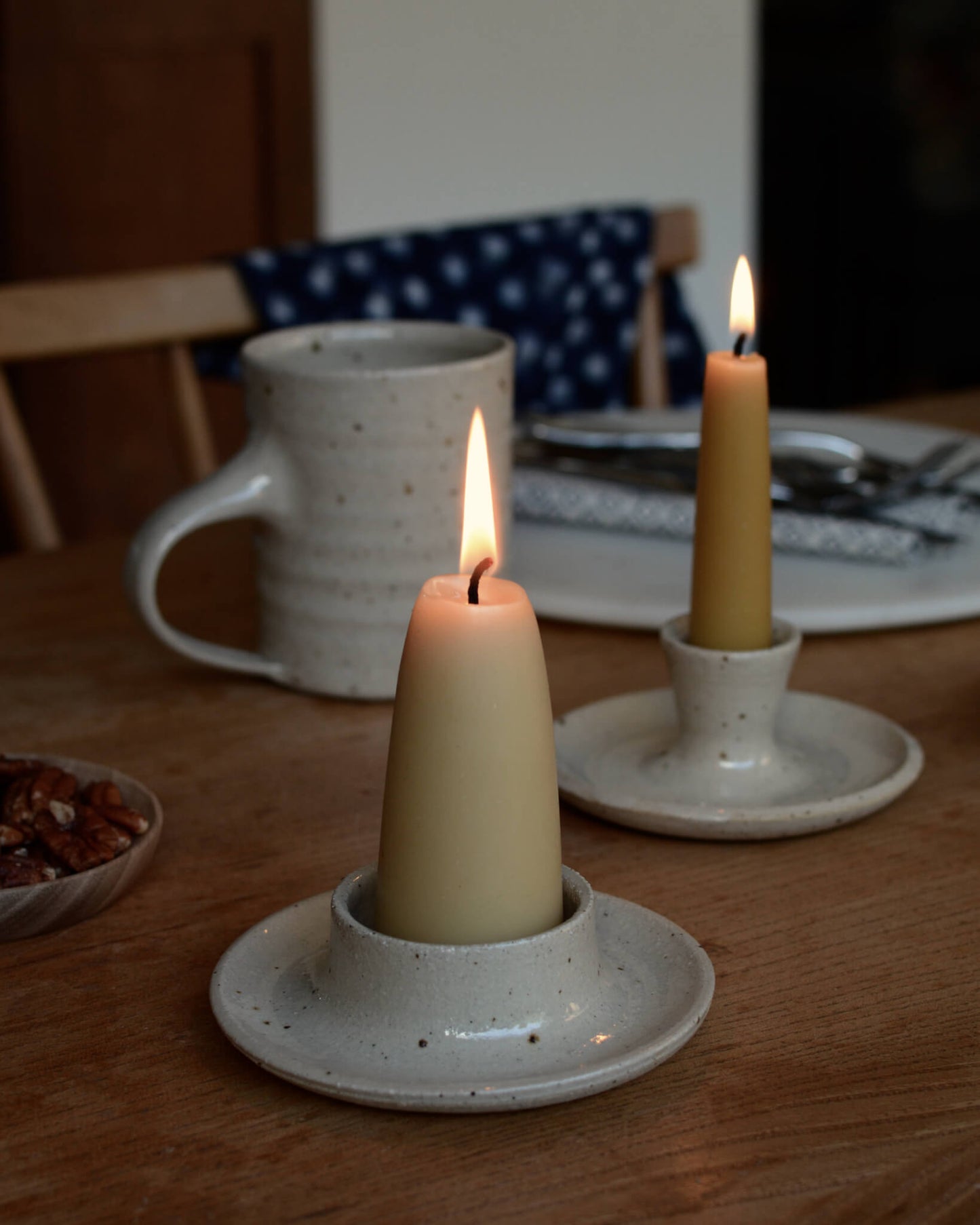 Beeswax candles and oatmeal ceramic pillar candle holders, on a wooden dining table.