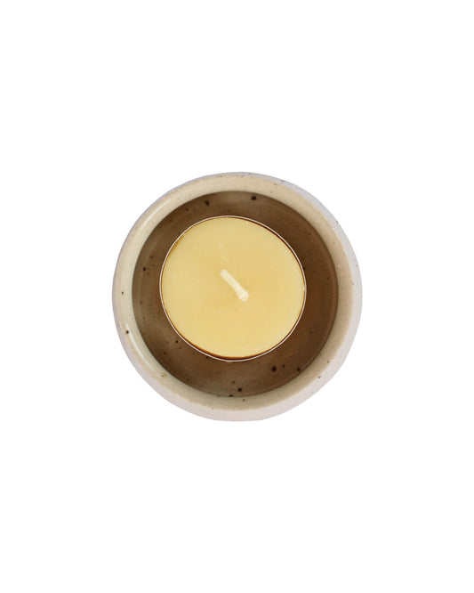 A ceramic tea light holder, on a white background, shown with a beeswax candle.