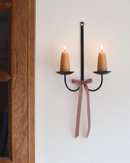 A metal wall-mounted candle holder with stubby beeswax candles and a velvet bow beneath.