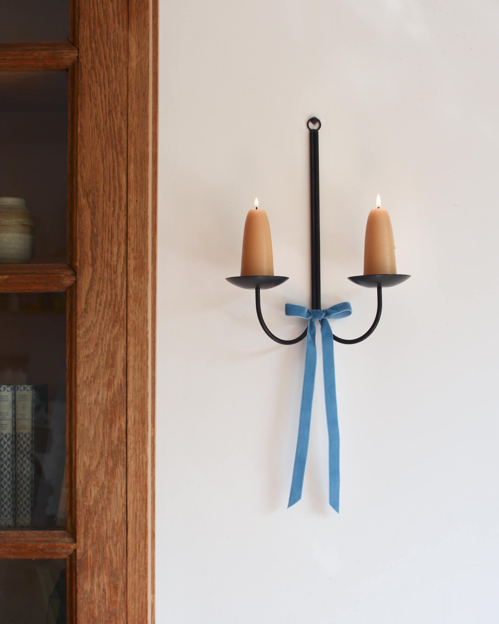 A metal wall-mounted candle holder with stubby beeswax candles and a velvet bow beneath.