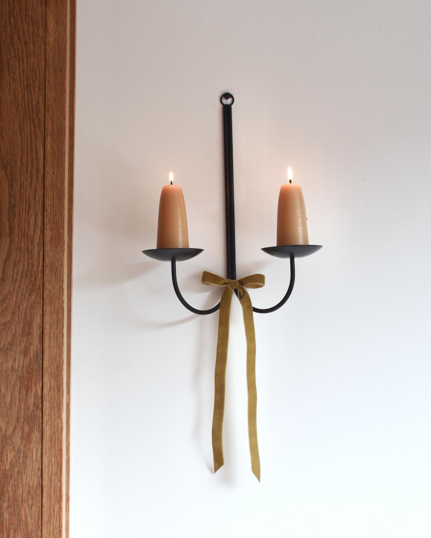 A metal wall-mounted candle holder with stubby beeswax candles and a velvet bow beneath.