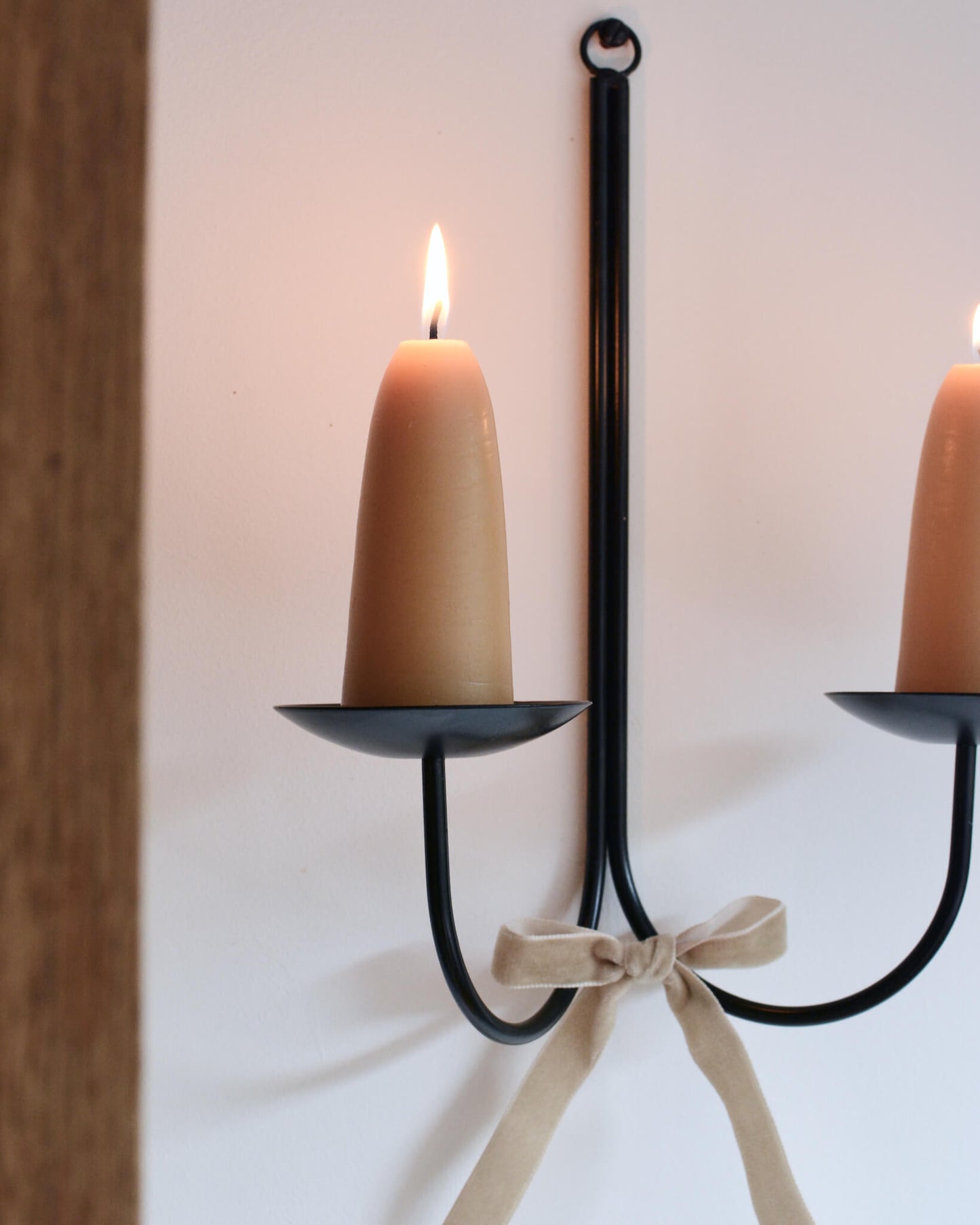 Close-up of a metal wall-mounted candle holder with stubby beeswax candles and a velvet bow beneath.