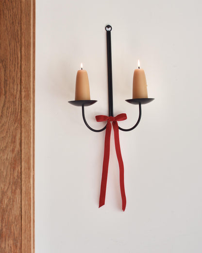 A metal wall-mounted candle holder with stubby beeswax candles and a velvet bow beneath.