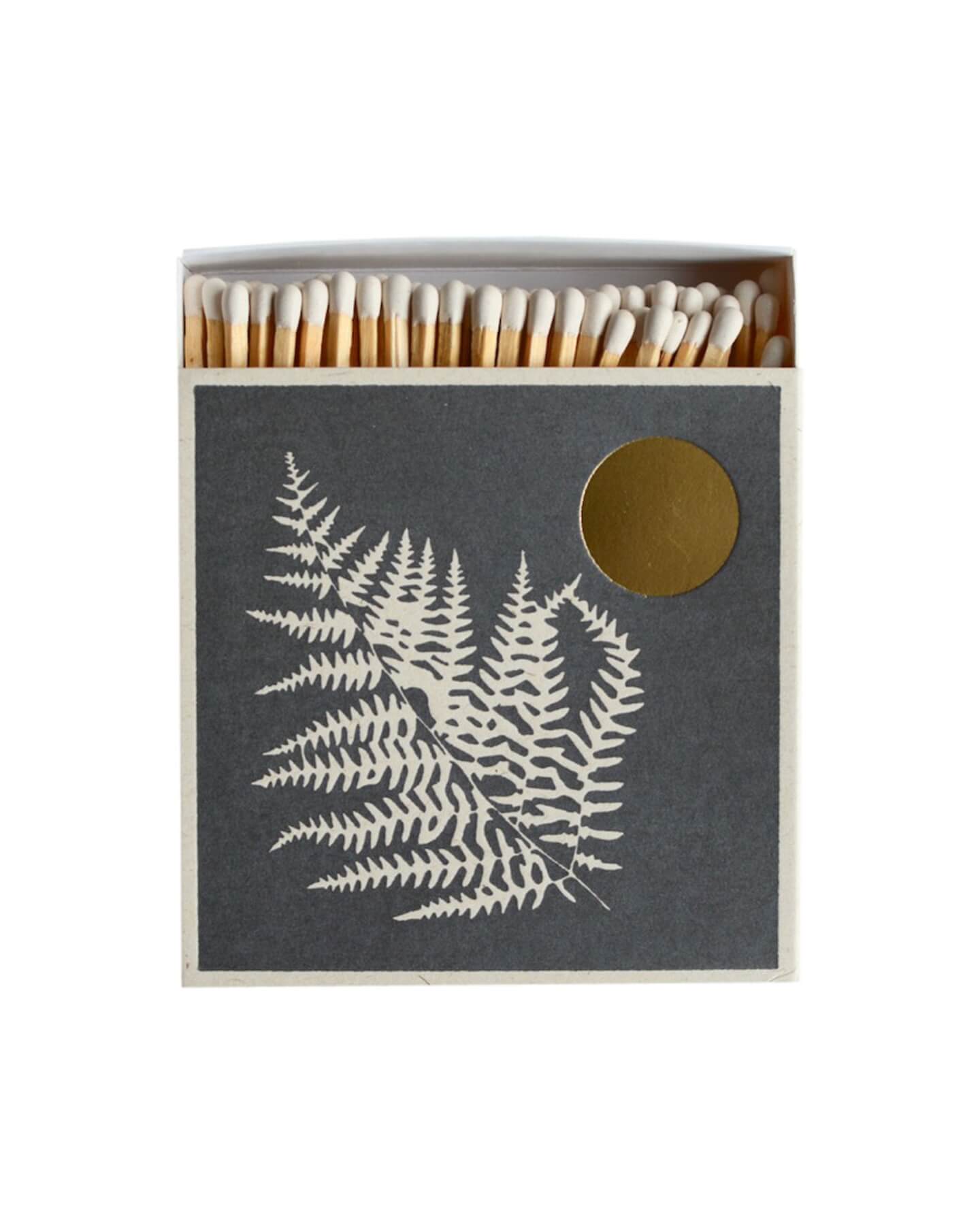 Dark grey match box with white fern leaf illustration and gold leaf moon.