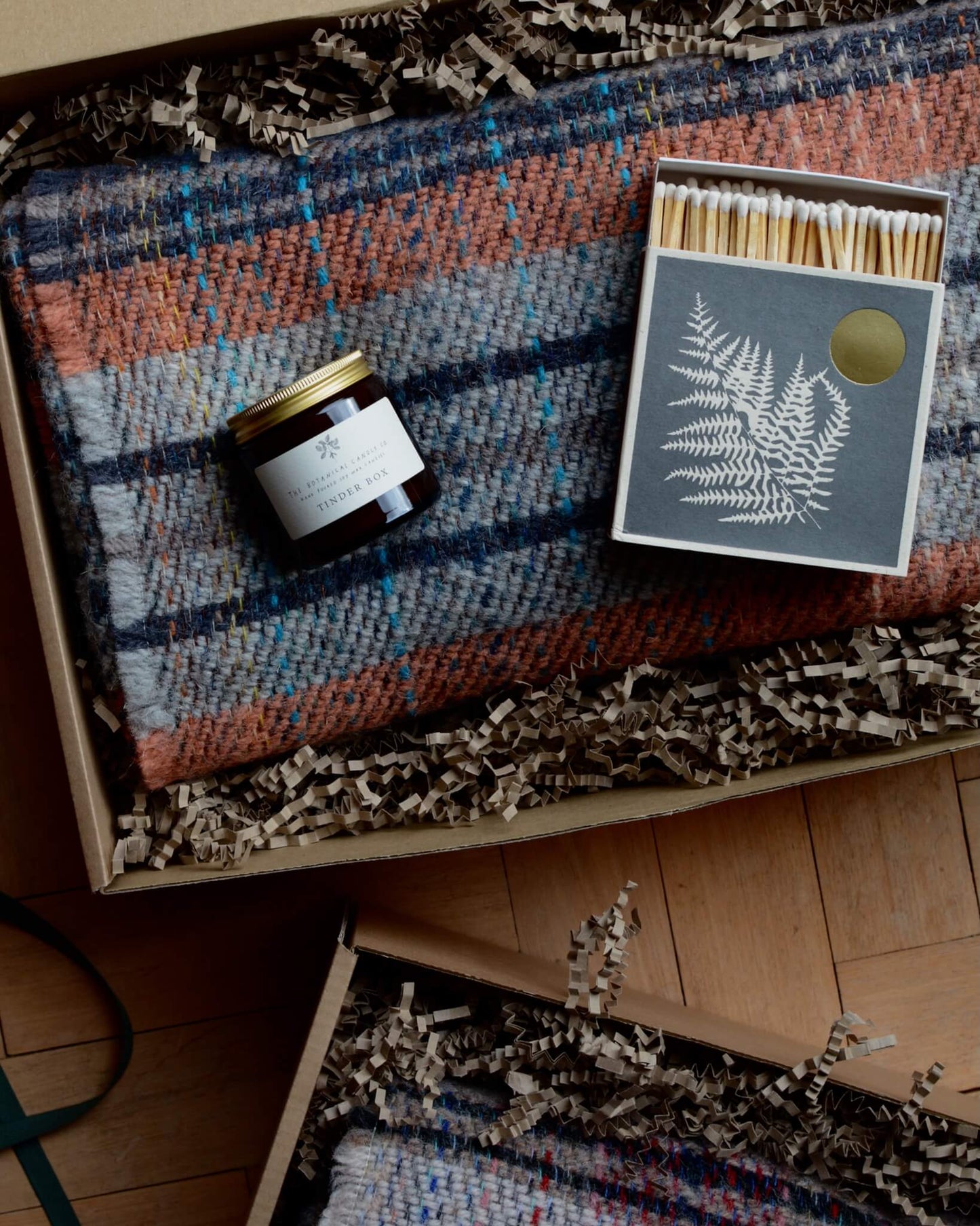 Dark grey match box on top of a checked woollen blanket.