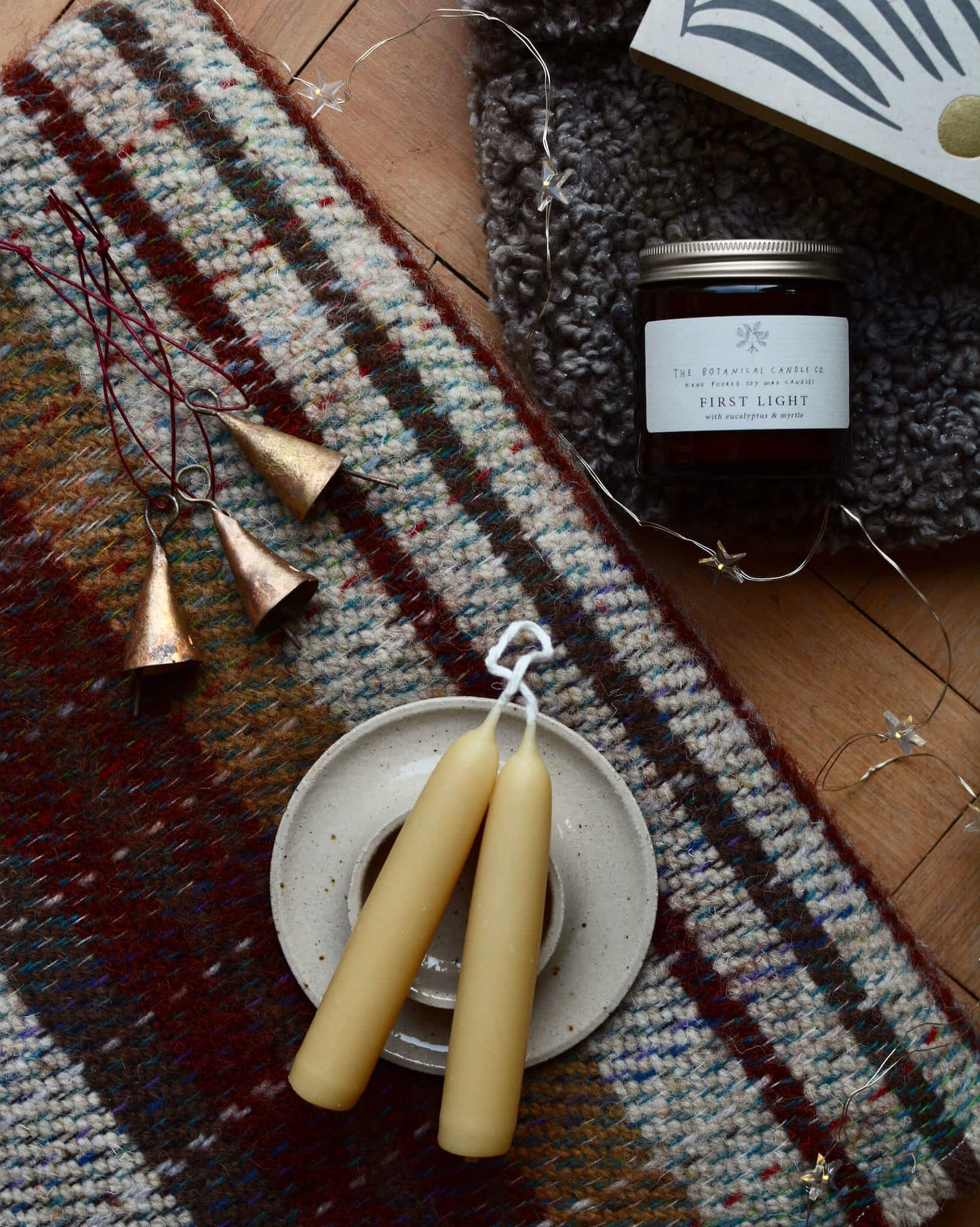 A winter blend soy candle next to a woollen blanket and beeswax candles.