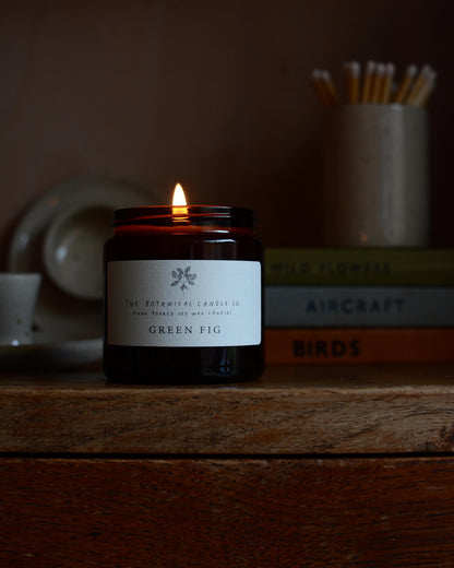 A lit scented candle, photographed on a wooden cabinet.