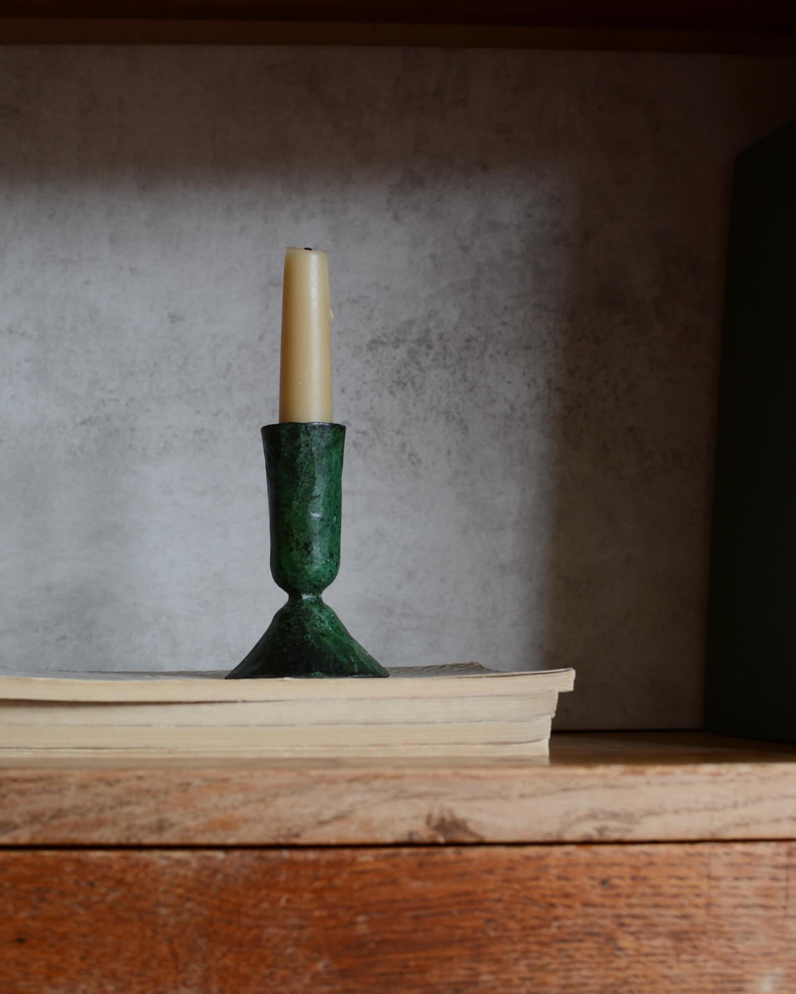 A metal taper candle holder, with a green verdigris finish.