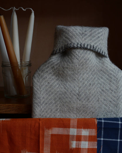 A grey wool hot water bottle, next to bright fabrics and beeswax candles.