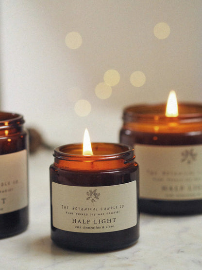 A 120ml winter blend clementine and clove scented candle in an amber glass jar, surrounded by twinkly lights.