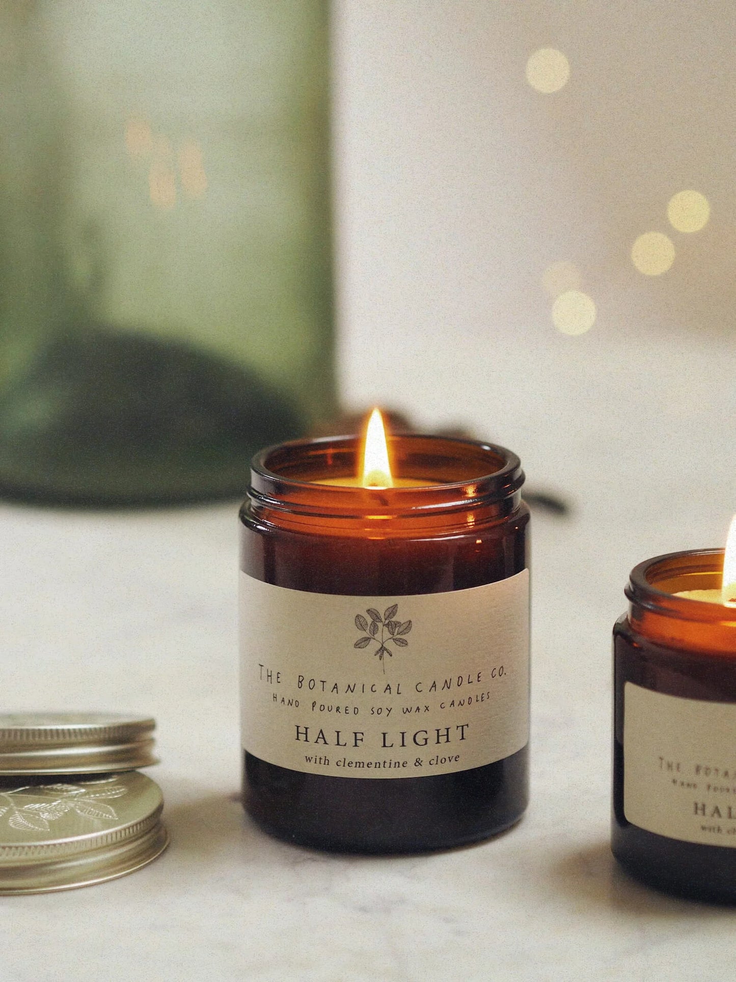 A 180ml winter blend clementine and clove scented candle in an amber glass jar, surrounded by twinkly lights.