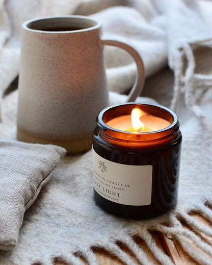 A winter blend cinnamon and clove scented candle in an amber glass jar, next to a coffee cup and woollen blanket.