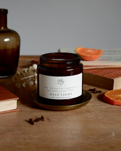 A winter blend clementine and clove scented candle in an amber glass jar, surrounded by cut clementines and cloves.