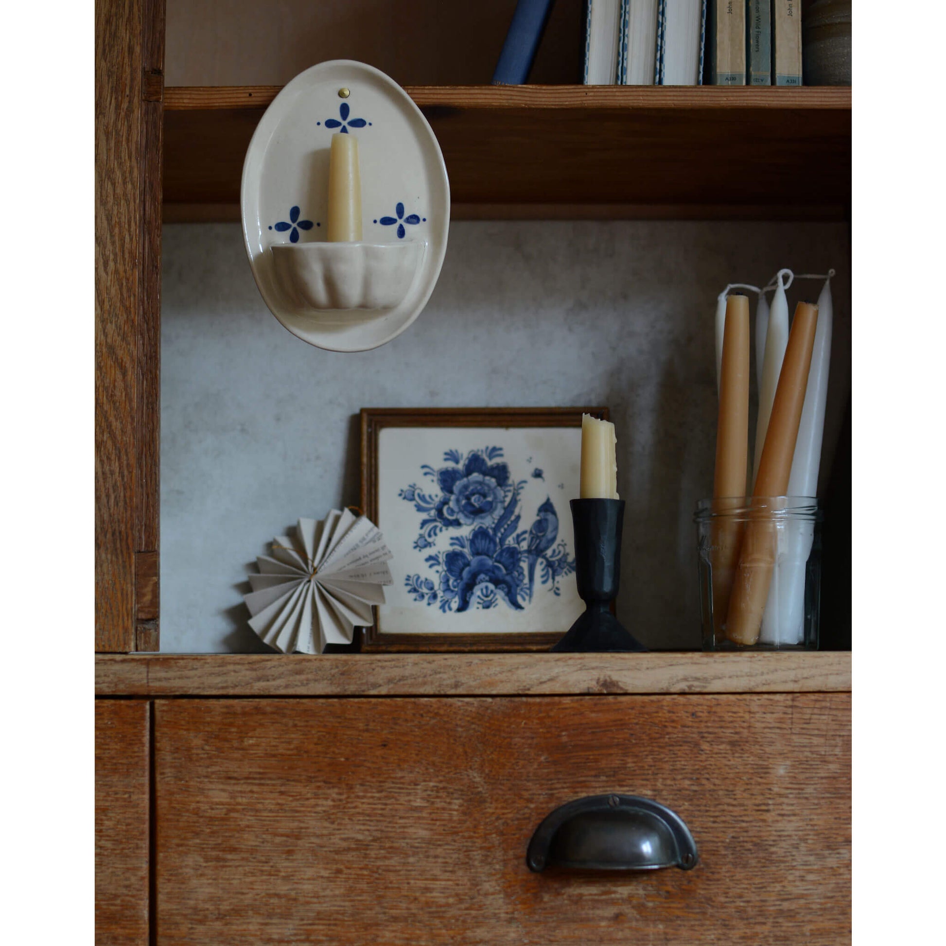 Cream and blue ceramic candle wall sconce, displayed with a beeswax candles, inside a wooden cabinet.