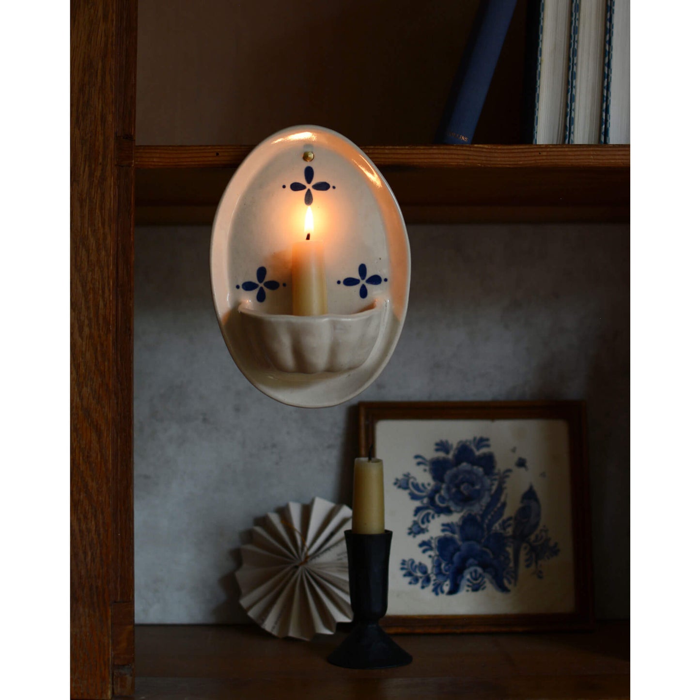 Cream and blue ceramic candle wall sconce, displayed with a beeswax candles, inside a wooden cabinet.