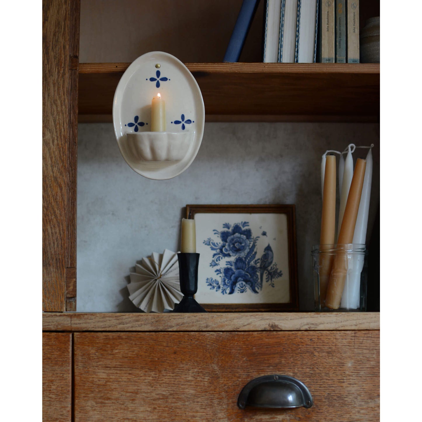 Cream and blue ceramic candle wall sconce, displayed with a beeswax candles, inside a wooden cabinet.