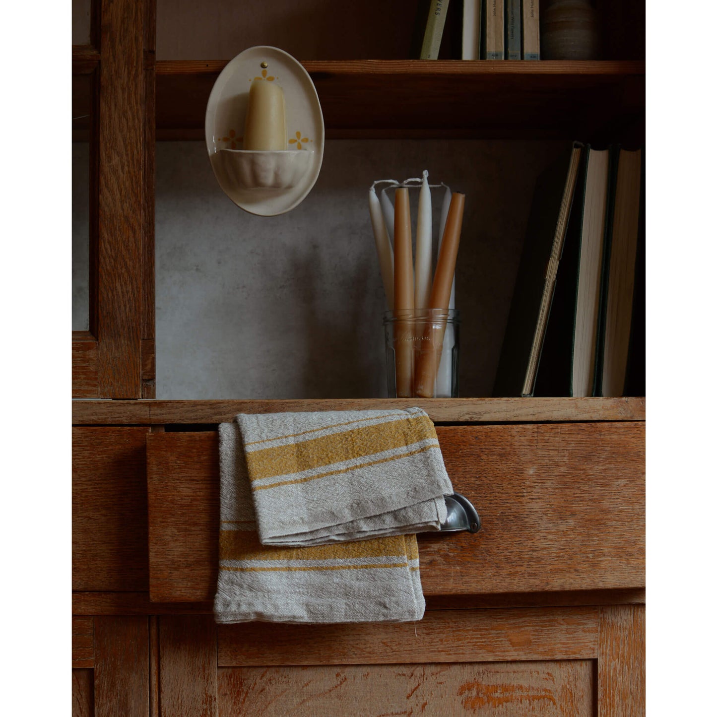 A cream and yellow ceramic candle holder and beeswax candles, on a wooden cabinet.