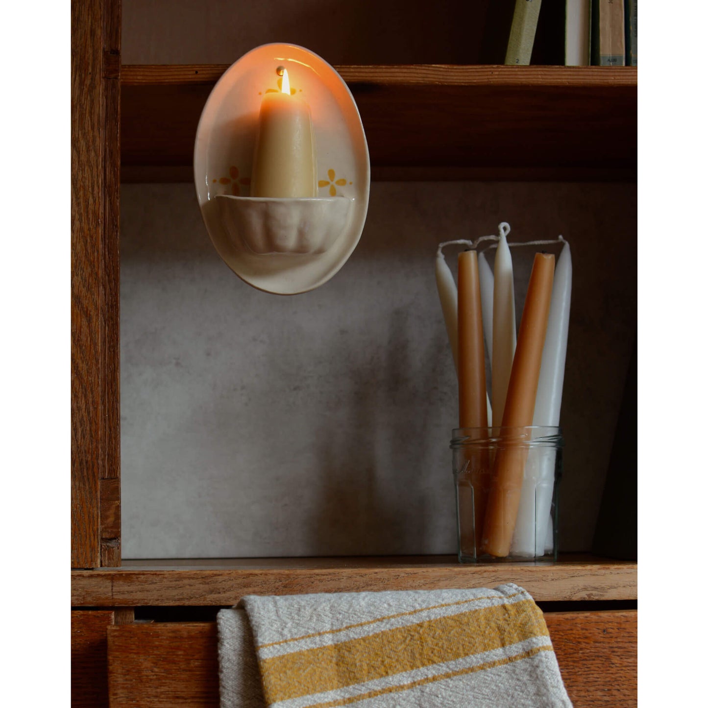 A cream and yellow ceramic candle holder and beeswax candles, on a wooden cabinet.