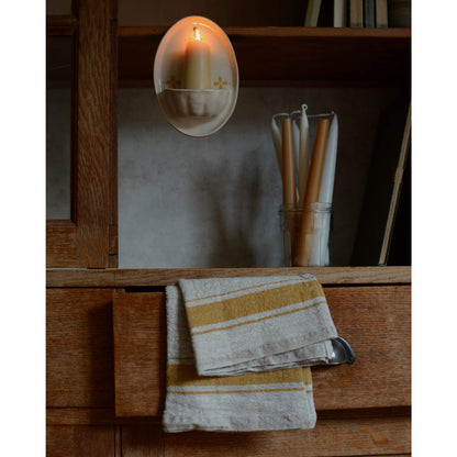 A cream and yellow ceramic candle holder and beeswax candles, on a wooden cabinet.