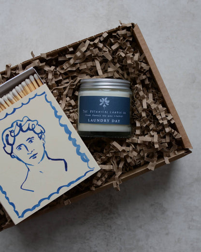 Illustrated square match box, next to a blue jar candle, in a gift box.