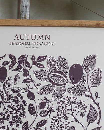 A linocut print in plum tones, depicting seasonal plants of Autumn. 