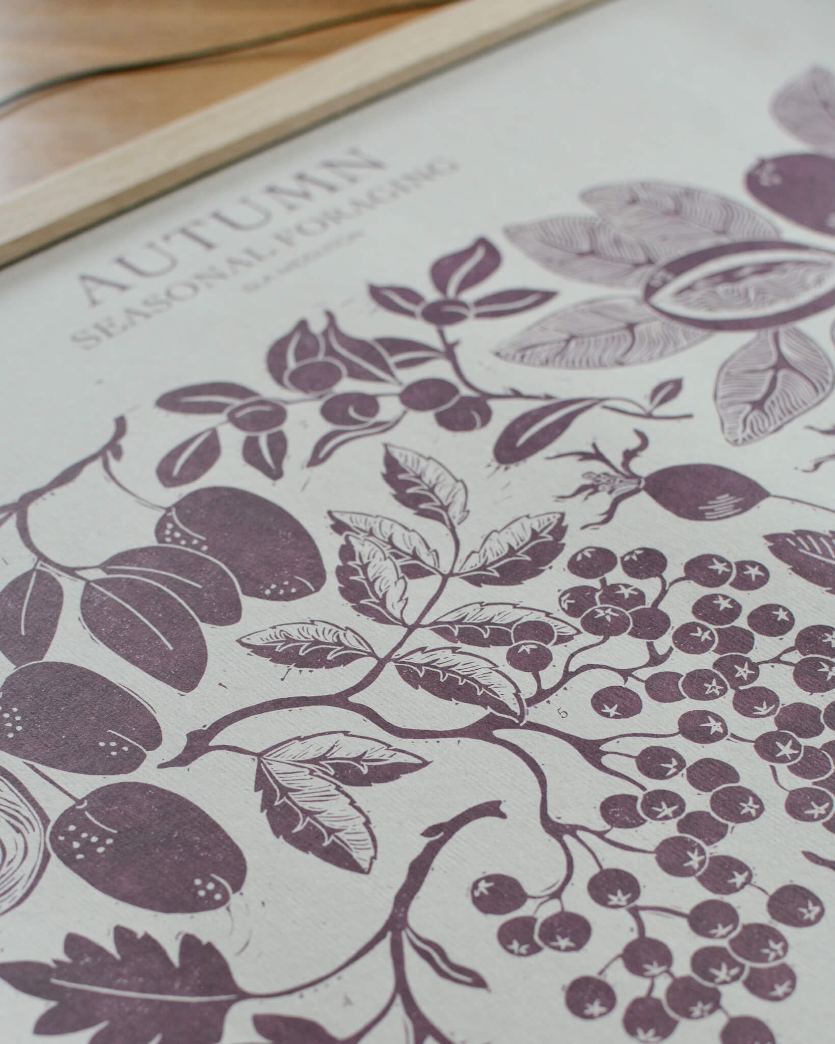 A linocut print in plum tones, depicting seasonal plants of Autumn. 