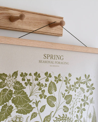 A green botanical print, depicting Spring plants. Hanging in an oak frame from an oak peg rail.