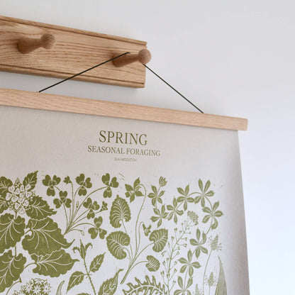 Botanical 'Spring' print with green ink on pale grey paper, hanging from an oak poster frame on a set of oak wall hooks.