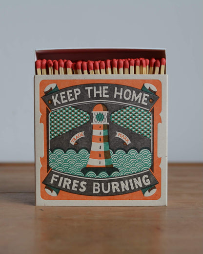 A letterpress design match box with an illustration of a lighthouse and the words 'keep the home fires burning'.